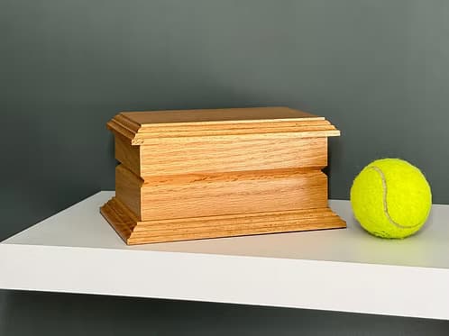 Solid oak pet ashes casket beside a tennis ball